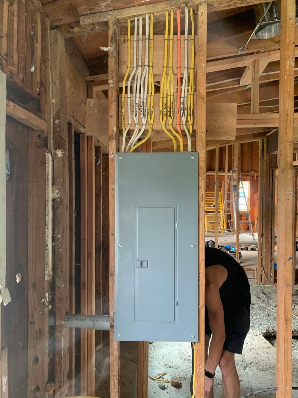 Electrical panel installation in a home renovation with visible wiring and open construction.